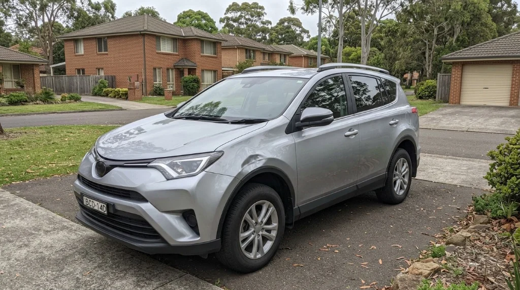 A silver Toyota RAV4 photographed whole on a driveway showing where the front fender damage sits.